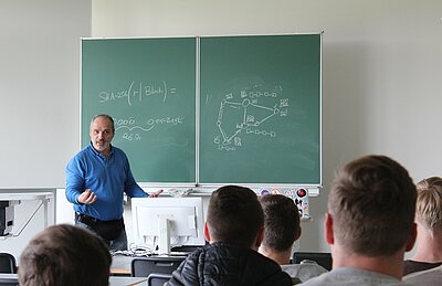 Lehrender vor Tafel mit einem Kurs Studierender