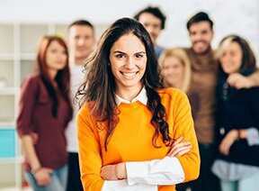 Studierende mit verschränkten Armen und lachen mit weiteren Personen im Hintergrund