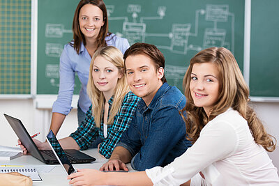 Studierende sitzen mit Laptops am Tisch im Hintergrund sieht man eine grüne Tafel